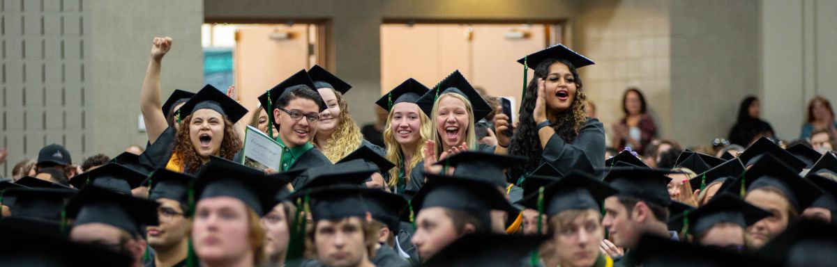 Students sitting at commencement with small group standing up and cheering