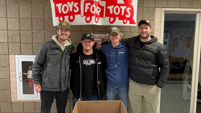 Four students in front of Toys for Tots sign