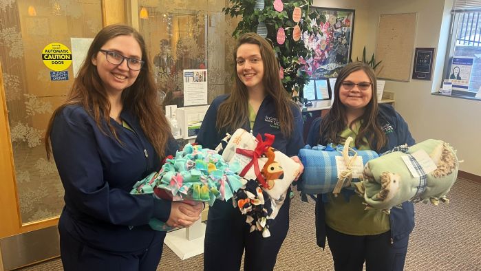 3 nursing students holding blankets smiling at camera