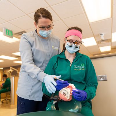 instructor guides dental hygiene student in practicing techniques