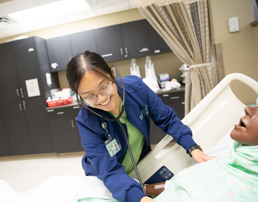 student practicing use of stethoscope on training mannequin 