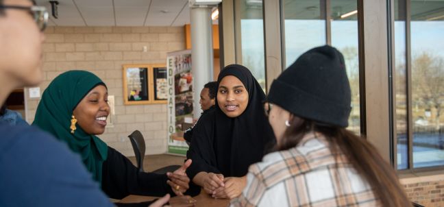 trio students talking while at a table near door 1