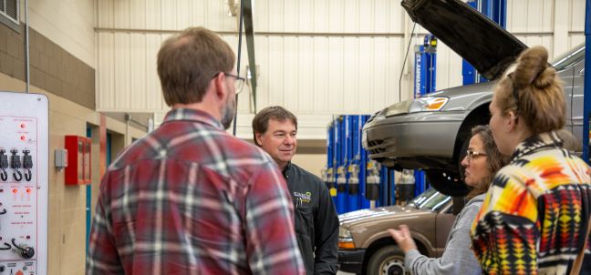 group of people talking with car on lift in background