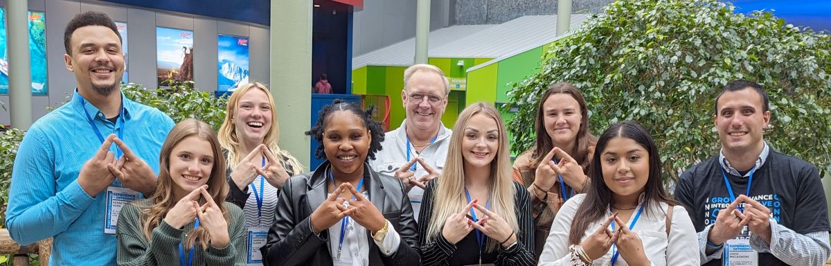 DECA team members in group, smiling at camera with DECA hand sign