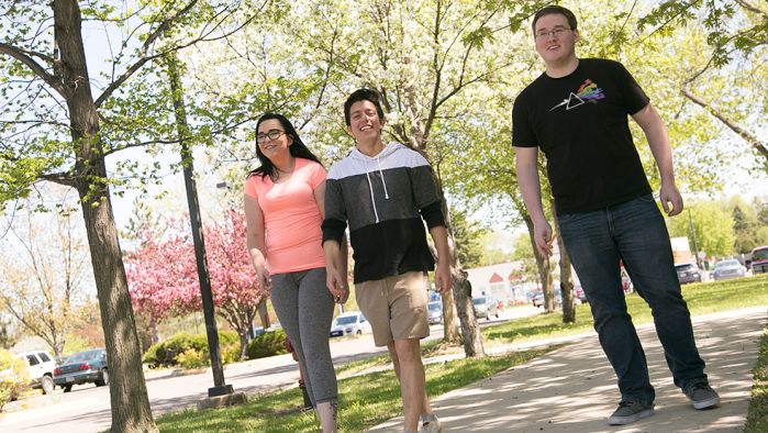 three students walking outside with a background of trees