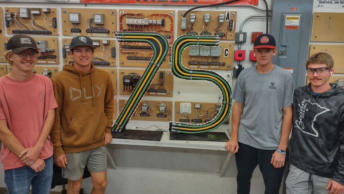 4 students standing next to 75 made of conduit