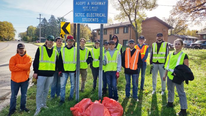 students in hi-vis vests in front of adopt-a-highway sign