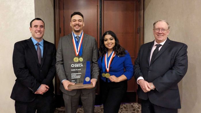 four deca members smiling at camera with awards