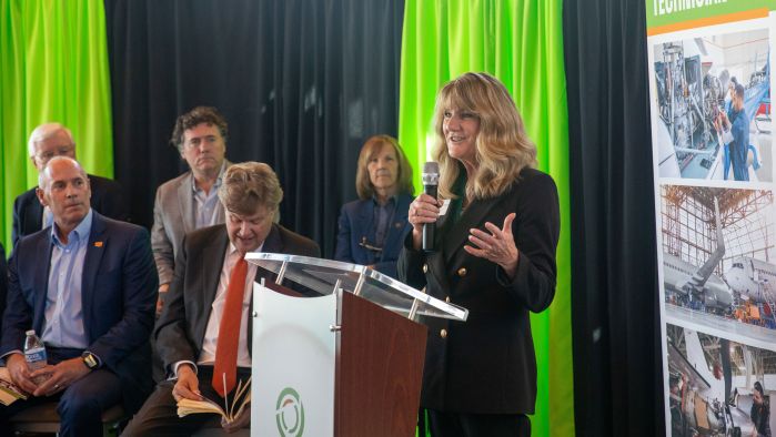 President Kloos speaks at a podium with other speakers sitting behind her