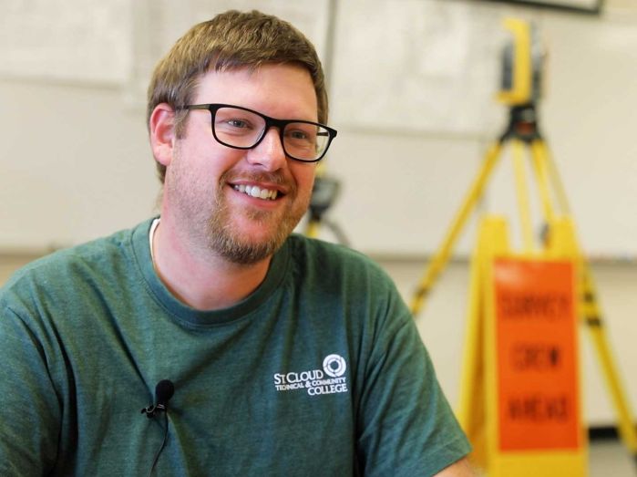 Jacob Mackedanze smiling at camera with land survey equipment behind him