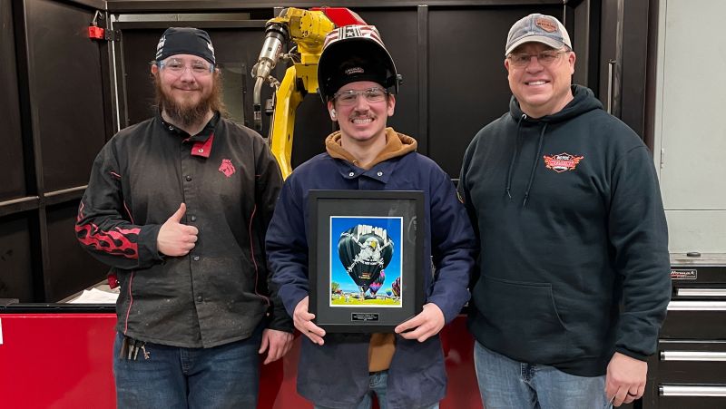 Two students and instructor holding plaque in front of robot