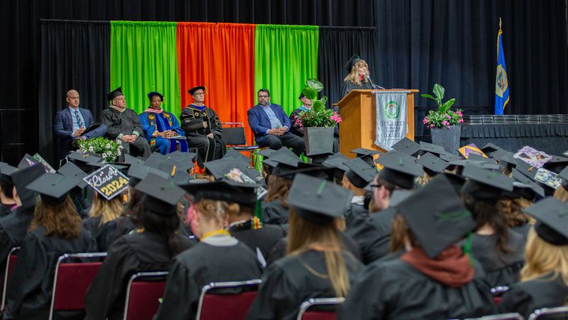 Lori Kloos speaking at podium to graduates at commencement