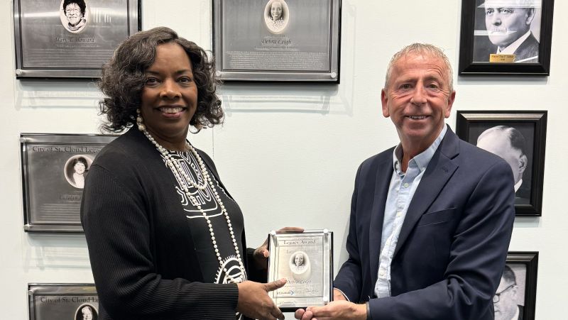 Debra Leigh and Mayor holding the award together in front of wall of awards