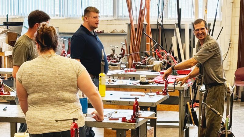 three HS teachers in plumbing lab with instructor Steve showing them a pipe