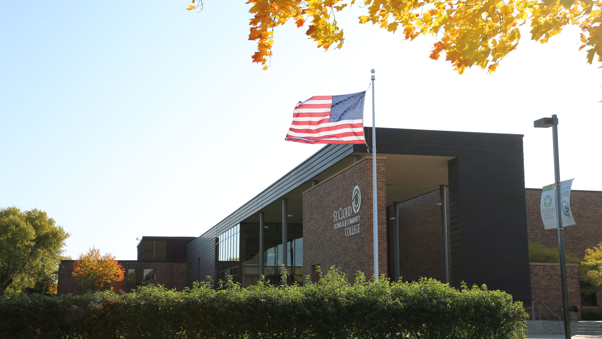 SCTCC main entrance with flag blowing in wind and yellow leaves at edge of image