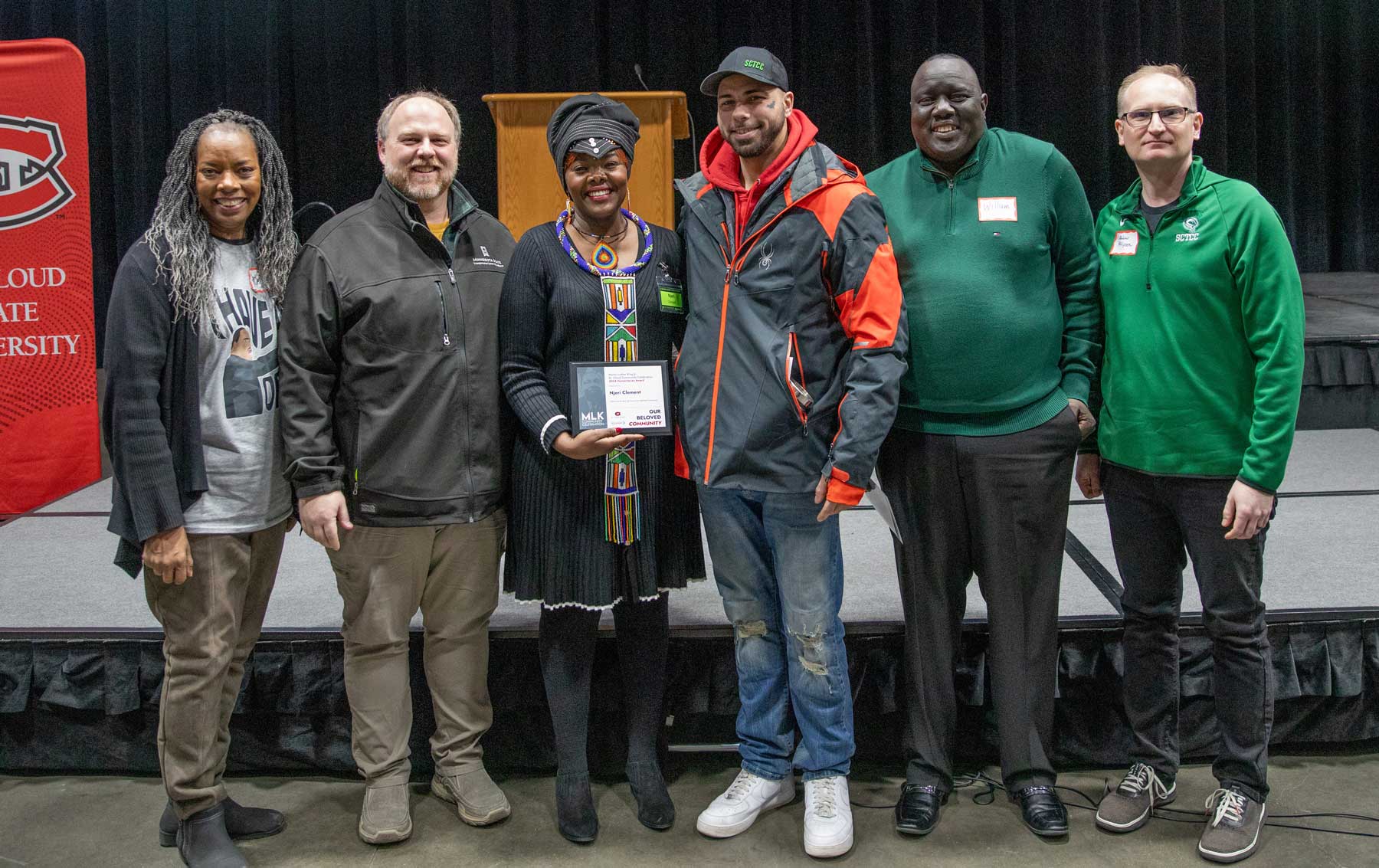 Six people including Njeri smiling at camera in front of stage